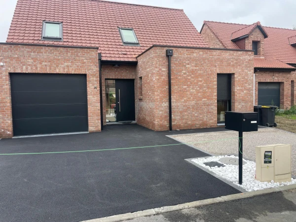 Allée de garage en enrobé noir à chaud et maison moderne en brique